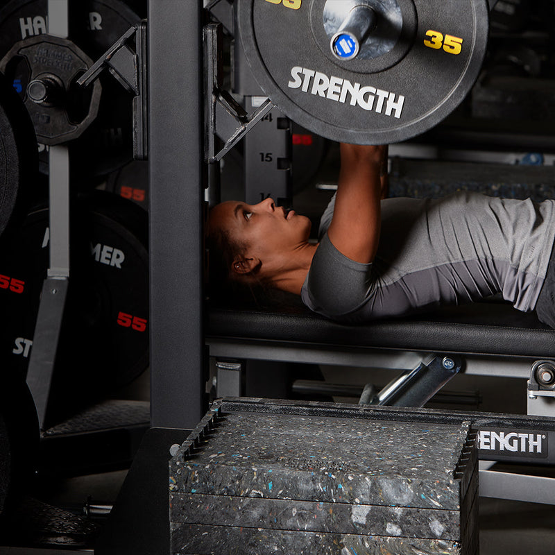 Female bench pressing 35LB urethane bumper plates